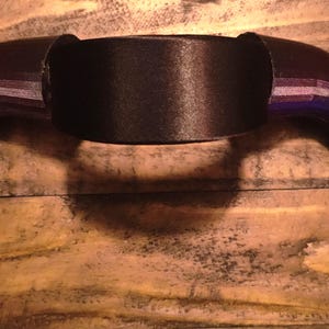 K&ouml;nnte beinhalten: Ein schwarzes, gebogenes hornf&ouml;rmiges Kopfst&uuml;ck mit einem Mittelband. Die H&ouml;rner haben einen Farbverlauf, einschlie&szlig;lich Lila und Blau. Das Kopfst&uuml;ck ist wahrscheinlich f&uuml;r Cosplay oder Kost&uuml;me gedacht.