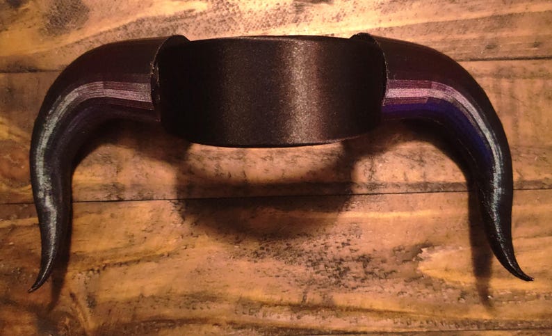 K&ouml;nnte beinhalten: Ein schwarzes, gebogenes hornf&ouml;rmiges Kopfst&uuml;ck mit einem Mittelband. Die H&ouml;rner haben einen Farbverlauf, einschlie&szlig;lich Lila und Blau. Das Kopfst&uuml;ck ist wahrscheinlich f&uuml;r Cosplay oder Kost&uuml;me gedacht.