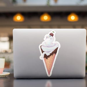 Op de afbeelding: Een witte slang opgerold in een wafeltje met een kers op de top. De slang is omringd door wit ijs en chocoladesaus.