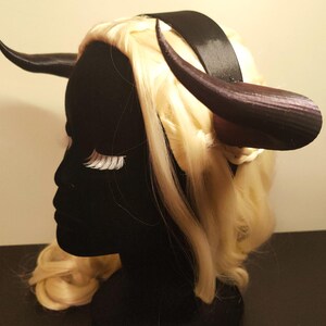 K&ouml;nnte beinhalten: Ein schwarzes Kopfst&uuml;ck mit dunkelvioletten H&ouml;rnern und einem schwarzen Stirnband. Das Kopfst&uuml;ck ist mit blondem Haar und wei&szlig;en Wimpern geschm&uuml;ckt. Dieses Kost&uuml;mzubeh&ouml;r ist ideal f&uuml;r Cosplay oder Themenveranstaltungen.