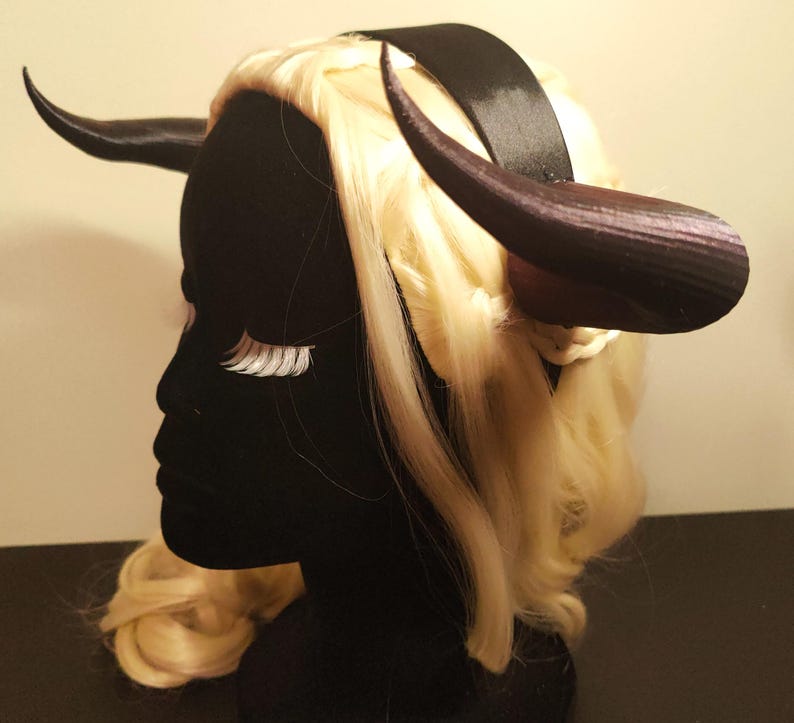 K&ouml;nnte beinhalten: Ein schwarzes Kopfst&uuml;ck mit dunkelvioletten H&ouml;rnern und einem schwarzen Stirnband. Das Kopfst&uuml;ck ist mit blondem Haar und wei&szlig;en Wimpern geschm&uuml;ckt. Dieses Kost&uuml;mzubeh&ouml;r ist ideal f&uuml;r Cosplay oder Themenveranstaltungen.