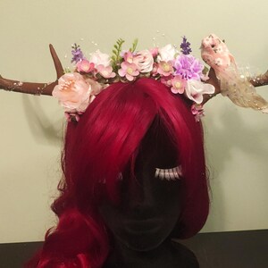 May include: A brown antler headband with pink, white, and purple flowers and a pink bird decoration.