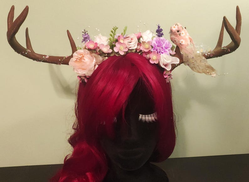 May include: A brown antler headband with pink, white, and purple flowers and a pink bird decoration.