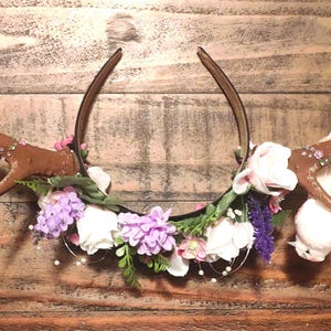 May include: A headband with a brown antler design and a floral garland with white and purple flowers.