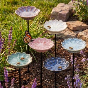 Peut inclure: Un ensemble de six tuteurs de jardin en céramique en forme de fleur, déclinés en violet, blanc, rose, bleu clair, bleu sarcelle et bleu foncé. Chaque tuteur comporte un bassin peu profond pour l'eau, avec un papillon monarque et des abeilles.