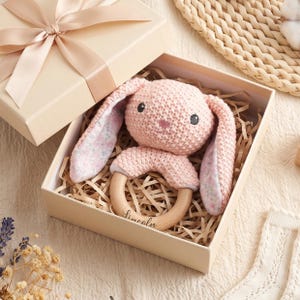 Peut inclure: Un hochet lapin en crochet rose pâle avec de longues oreilles doublées de tissu floral, fixé à un anneau en bois lisse gravé du prénom Lincoln. Le hochet est présenté dans une boîte cadeau beige avec un ruban en satin assorti.