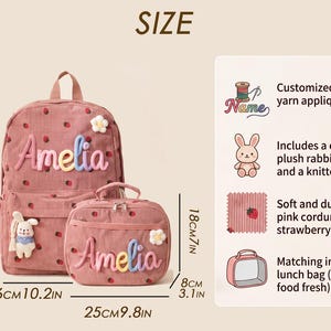 May include: A pink corduroy backpack and matching lunch bag with a strawberry pattern, featuring the name Amelia in colorful yarn applique, a plush rabbit charm, and a knitted daisy. The backpack measures 15.3 inches by 10.2 inches by 5.1 inches.