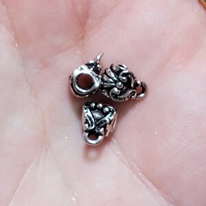 May include: Three silver metal bead caps with ornate designs. The caps have a hole in the center for stringing.