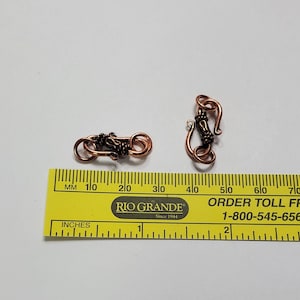 May include: Two copper-colored clasps for jewelry making, each measuring approximately 2 inches in length. The clasps are made of wire that is twisted and looped to create a unique design.