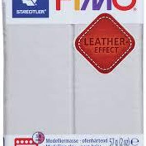 May include: A rectangular package of white Fimo oven-bake modelling clay by Staedtler. The packaging features the Fimo logo, a red diamond-shaped label reading Leather Effect, and text indicating a weight of 57 grams or 2 ounces.