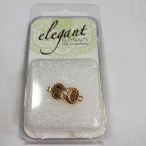 May include: Gold-tone infinity symbol clasp with clear rhinestones. The clasp is packaged in a clear plastic container with the words "elegant elements elite components" on the label.