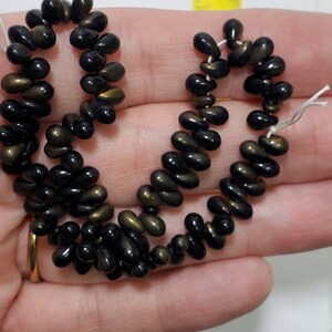 May include: A strand of black and gold glass beads. The beads are teardrop shaped and have a glossy finish.