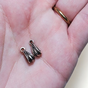 May include: Two silver-toned pendant bails with a decorative design. The bails are small and have a teardrop shape.