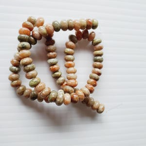 Puede incluir: Hilo de cuentas de piedras preciosas en tonos naranja, verde y crema. Las cuentas de forma ovalada están ensartadas, creando un componente de collar o pulsera. Las cuentas tienen un aspecto natural y terroso.