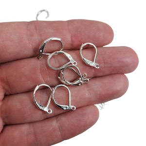 May include: Several silver-colored leverback earring findings are displayed. These findings have a curved, hinged design with a small loop at the bottom for attaching earrings. The findings are shown against a white background.