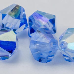 Puede incluir: Primer plano de varias cuentas de cristal azul claro facetadas. Las cuentas tienen una forma geométrica con múltiples facetas que reflejan la luz, creando un efecto brillante. Ideal para la fabricación de joyas.