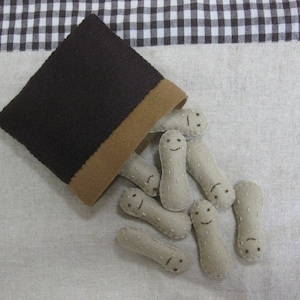 Puede incluir: Una bolsa de fieltro marrón con un forro de fieltro beige está derramando una colección de juguetes de cacahuete de fieltro. Cada cacahuete tiene una cara sonriente bordada.