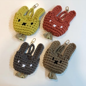 May include: Four crocheted bunny-shaped keychains with different colored yarn. The keychains are green, brown, red, and dark brown. Each keychain has a white face with black eyes and a black nose.