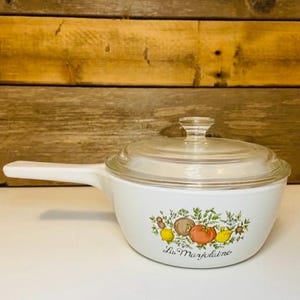 May include: White casserole dish with a clear glass lid and a long handle. The dish features a colorful illustration of vegetables and the text "La Marjolaine".