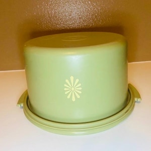 Peut inclure: Un porte-gâteau vert clair avec une base et un couvercle assortis. Le couvercle présente un motif floral jaune pâle. Le support a une forme arrondie et des poignées sur la base pour faciliter le transport. Un article de cuisine classique.