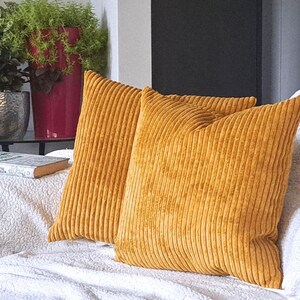 May include: Two mustard yellow corduroy throw pillows with a ribbed texture. The pillows are on a white couch.