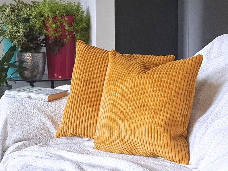 May include: Two mustard yellow corduroy throw pillows with a ribbed texture. The pillows are on a white couch.