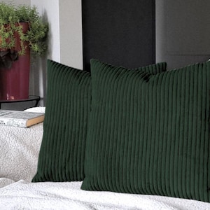 May include: Two dark green corduroy throw pillows with a ribbed texture. The pillows are on a white couch.
