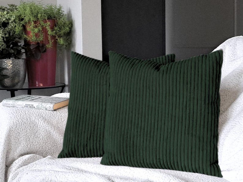 May include: Two dark green corduroy throw pillows with a ribbed texture. The pillows are on a white couch.