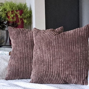 May include: Two brown corduroy throw pillows with a vertical ribbed texture. The pillows are on a white couch.