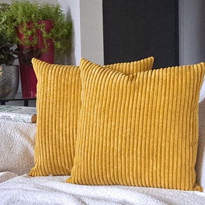 May include: Two mustard yellow corduroy throw pillows with a ribbed texture. The pillows are on a white couch.