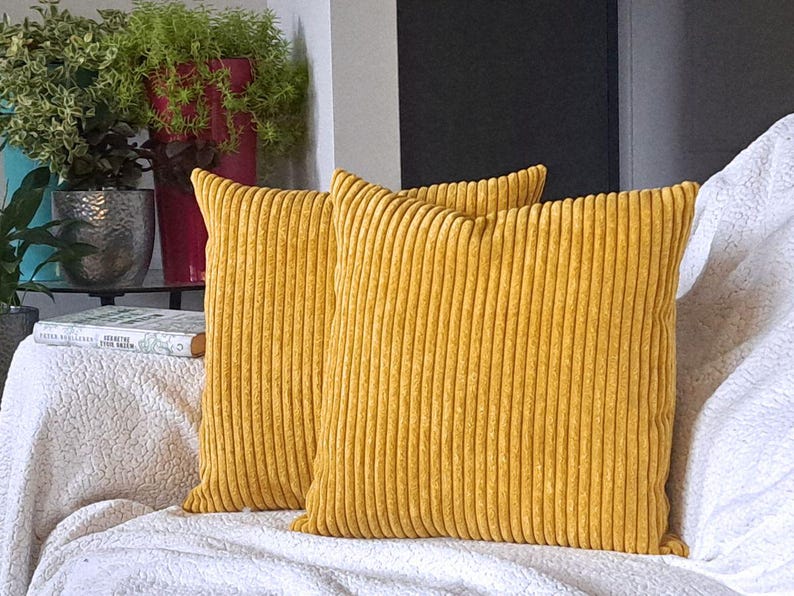 May include: Two mustard yellow corduroy throw pillows with a ribbed texture. The pillows are on a white couch.