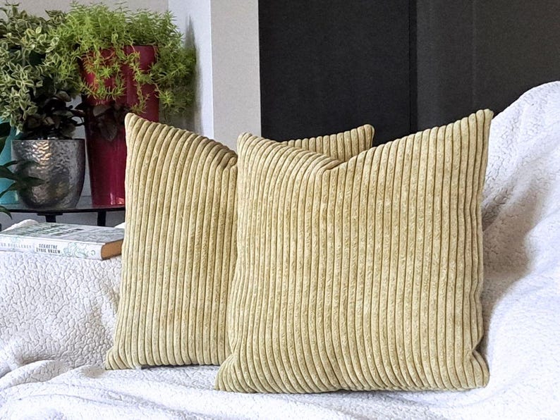May include: Two light green corduroy throw pillows with a ribbed texture. The pillows are on a white couch.