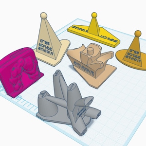 Puede incluir: Cinco objetos impresos en 3D, incluyendo un elefante rosa, un objeto gris con una hélice y tres objetos amarillos en forma de cono con texto que dice "STRAW HAT" y "0'92" en negro.