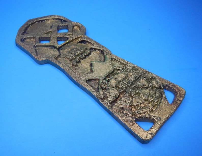 An angled view of the front of the Goonies Copper Bones Key showing detail of the round symbol at the bottom