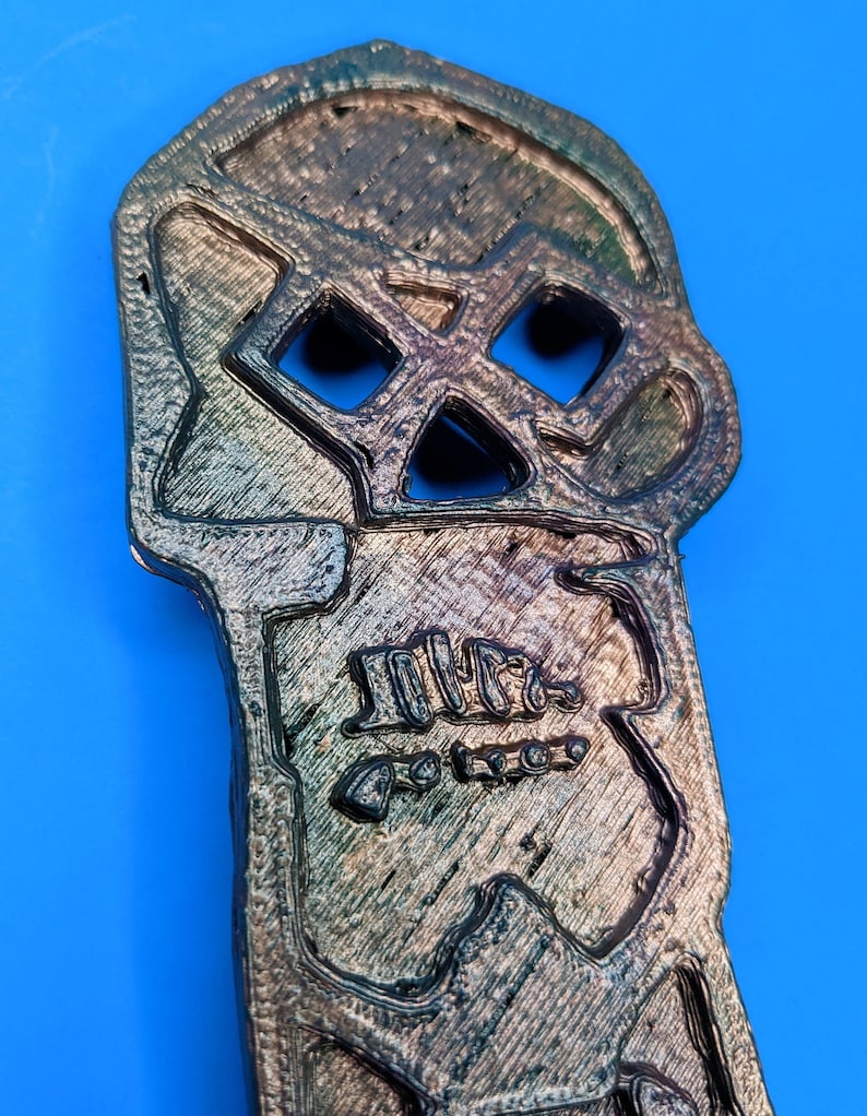 A detailed view of the top 'skull' portion of the copper bones key against a blue background
