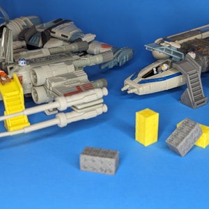 Peut inclure: Un ensemble de vaisseaux spatiaux jouets avec des détails gris, blancs et bleus. Les vaisseaux spatiaux sont sur une surface bleue avec des blocs de construction gris et jaunes.