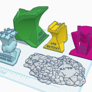 以下が含まれることがあります： 緑、黄色、ピンクなど、さまざまな色の3Dプリントされた幾何学的な形状のコレクション。形状にはテキストがあり、青いグリッド上に配置されています。灰色の岩のような構造も存在します。
