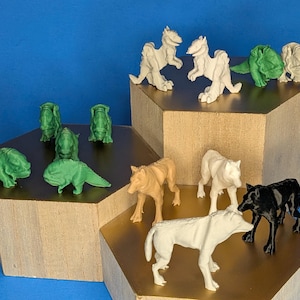 Könnte beinhalten: Eine Sammlung kleiner Tier- und Kreaturenfiguren aus Kunststoff in verschiedenen Farben wie Weiß, Grün, Beige und Schwarz. Das Set enthält wolfsähnliche Figuren und zweibeinige Reptilienmonster, die auf abgestuften sechseckigen Podesten stehen.