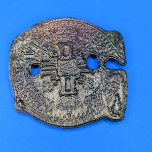 A 3D printed, gold-colored, irregularly shaped object with a design that resembles a cross with a circle in the center. The object has two holes and a notch on one side. The object is on a blue background.