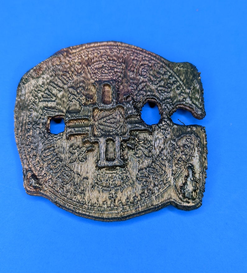 A 3D printed, gold-colored, irregularly shaped object with a design that resembles a cross with a circle in the center. The object has two holes and a notch on one side. The object is on a blue background.