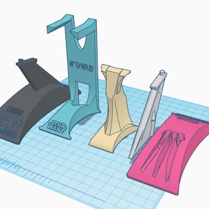 May include: Five 3D printed phone stands in different colors and designs. The stands are made of plastic and have a variety of shapes and sizes. The stands are all designed to hold a phone upright. The stands are all printed with the words "Star Wars" on them.