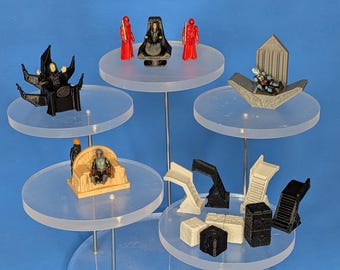 以下が含まれることがあります： 様々な玉座、階段、ブロック構造物を含む、プラスチック製のミニチュアフィギュアとアクセサリーのコレクション。このセットは、黒、赤、ベージュのキャラクターで構成されており、ディスプレイやテーブルトップゲーム用に詳細な成形デザインが施されています。