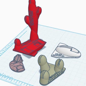 以下が含まれることがあります： テキストが刻まれた赤い3Dプリントのサボテン型オブジェクト、テキスト付きの白い楕円形のベース、小さな茶色のテクスチャ付きパーツ、テキスト付きのベージュの3本爪オブジェクトが、デジタルデザイン用の水色のグリッド作業面上に配置されています。