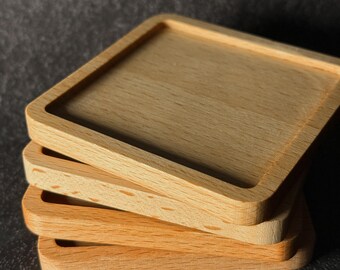 May include: A stack of four square wooden coasters. The coasters are made of light brown wood and have a slightly raised edge.