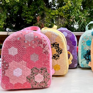 May include: Six colorful quilted backpacks with geometric patterns. The backpacks are made of fabric and have a variety of colors, including pink, yellow, green, blue, and brown.