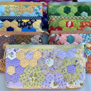 May include: A collection of handmade fabric pouches with a patchwork design. The pouches feature a variety of colors and patterns, including floral, geometric, and solid fabrics. Each pouch has a zipper closure and a small loop on the side.