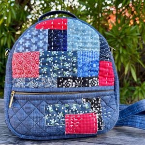 May include: A quilted patchwork backpack in shades of blue, red, and black. The bag features a top handle, a front zipper pocket, and adjustable straps. The patchwork design includes various floral and geometric patterns.