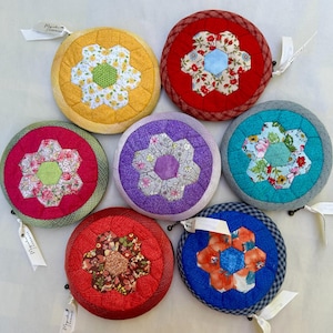 May include: Seven round fabric coin purses with a flower design in the center. The purses are in various colors including red, blue, yellow, purple, and teal.