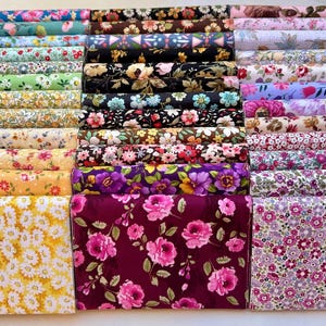May include: A stack of 24 fabric squares with various floral patterns in shades of pink, purple, yellow, green, and blue. The fabric squares are arranged in rows and are all approximately 6 inches by 6 inches.