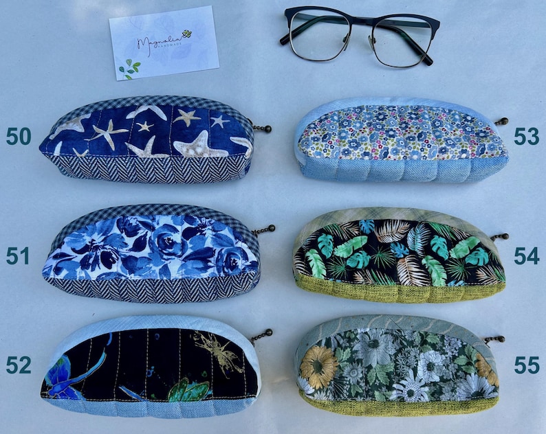 K&ouml;nnte beinhalten: Sechs halbkreisf&ouml;rmige Stoffetuis mit Rei&szlig;verschl&uuml;ssen, nummeriert von 50 bis 55, mit verschiedenen Mustern wie Seesternen, blauen Blumen, Libellen, kleinen Blumenprints, tropischen Bl&auml;ttern und Sonnenblumen, dazu eine Brille mit schwarzem Rahmen.